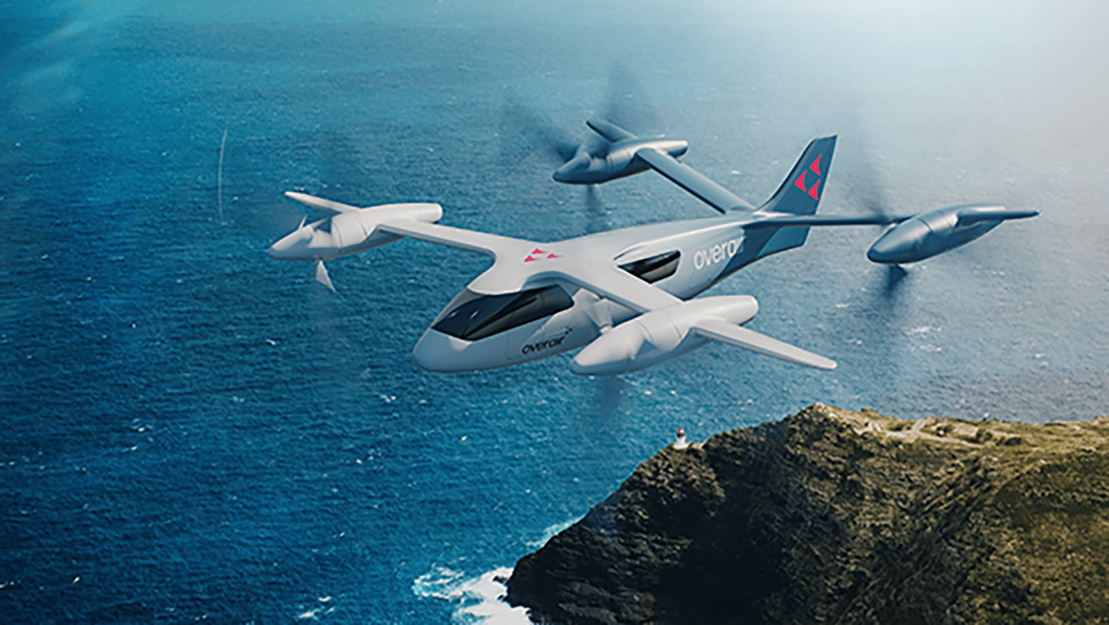 A sleek, white vertical takeoff and landing aircraft flies over a coastal cliff with the ocean beneath it.