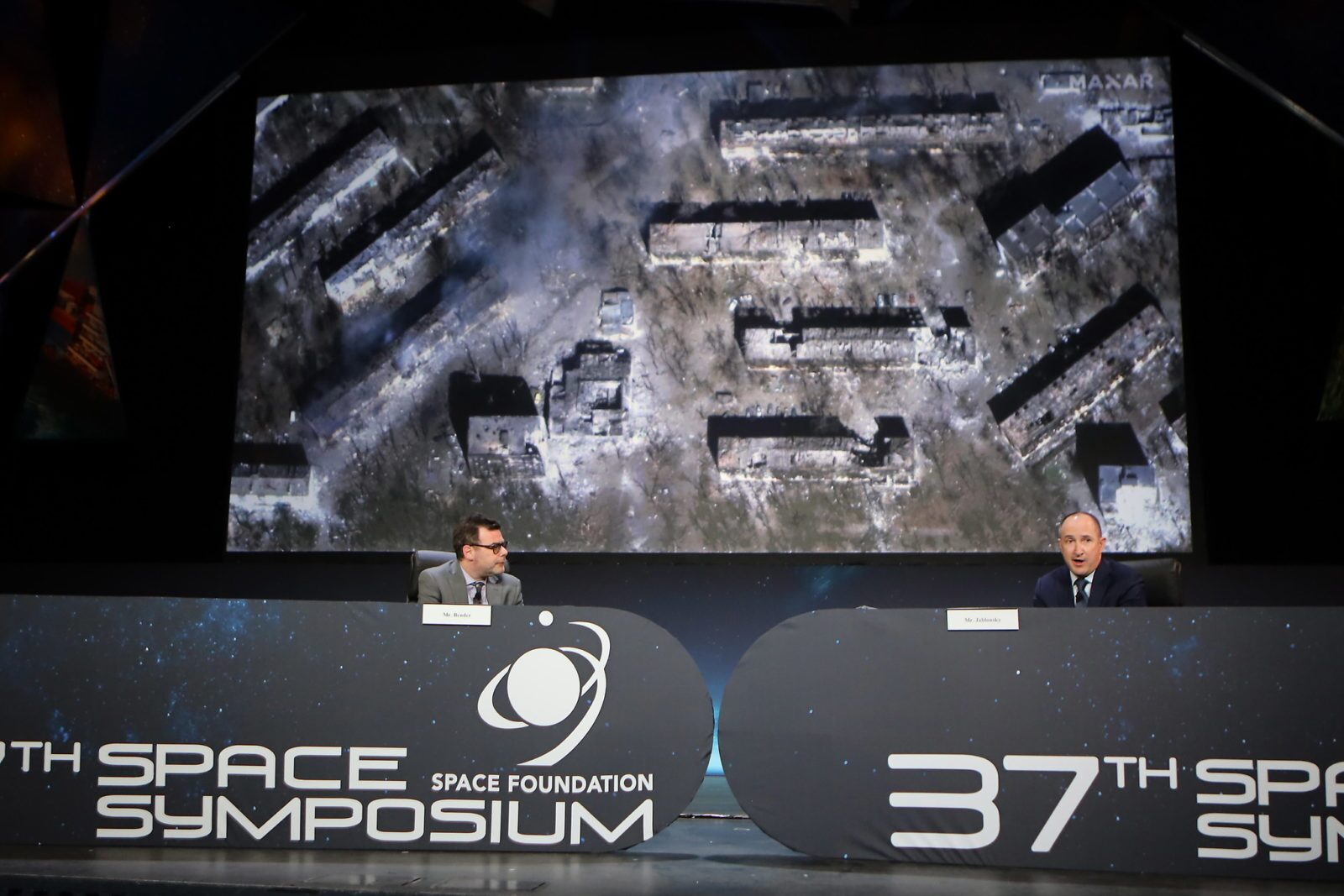 Two men sit behind a desk with the 