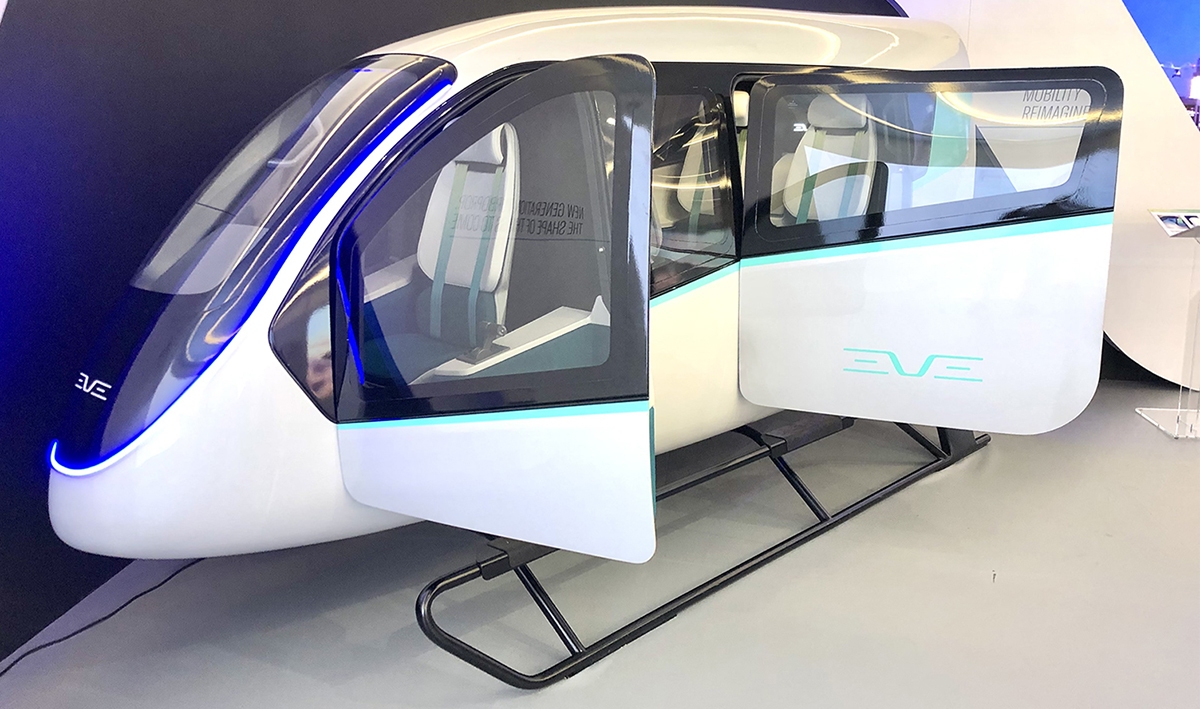 A futuristic, white eVTOL aircraft with open side doors and sleek blue accents is displayed indoors, showcasing an advanced and modern design.