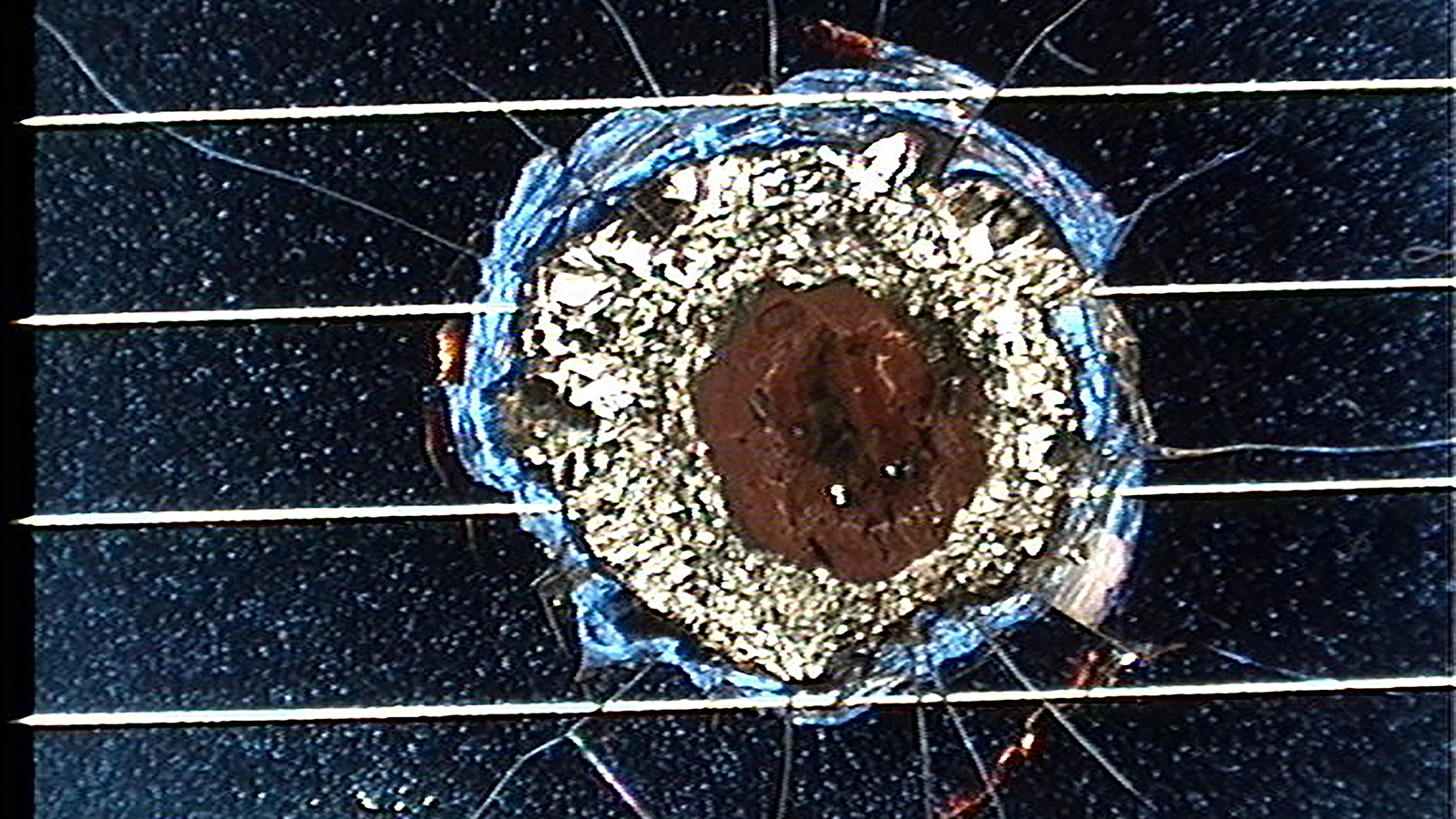 Close-up of a damaged guitar with a large, irregular hole on the top, surrounded by cracked wood and chipped paint, adjacent to several strings.