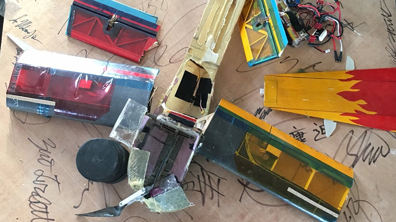 A collection of colorful, handmade model cars and planes, crafted from various materials, spread out on a table with scribbled notes.