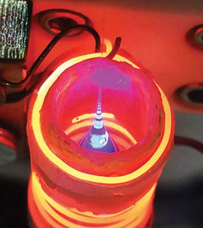 Glowing orange apparatus with wires attached surrounds a small pointed object emitting a bright blue light at the center.