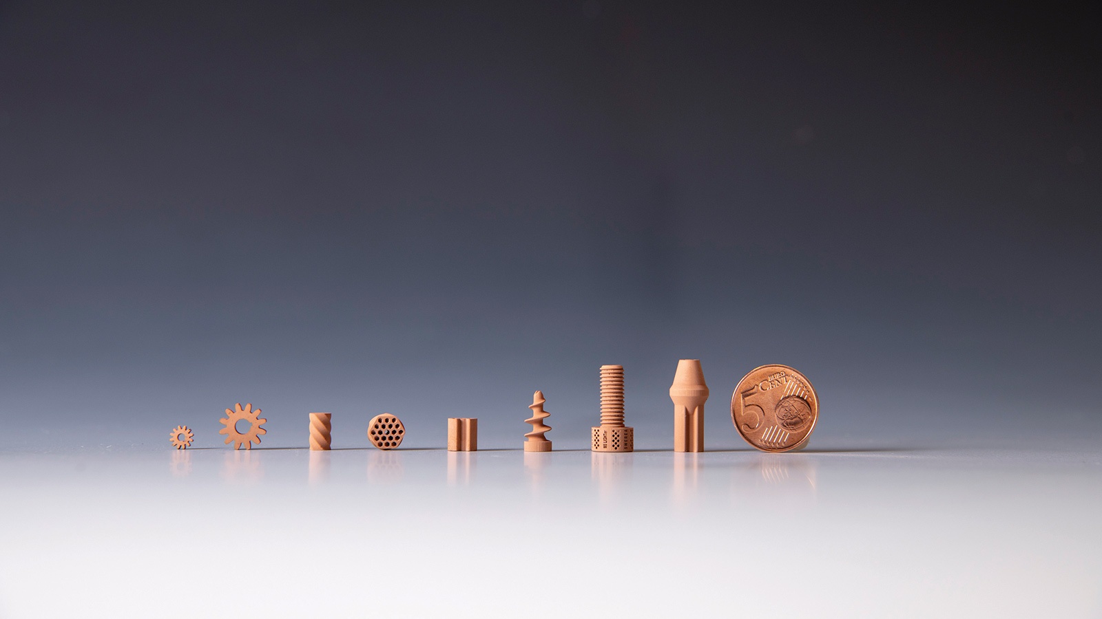 A row of small, intricately designed objects made from the same material, displayed next to a coin for scale.