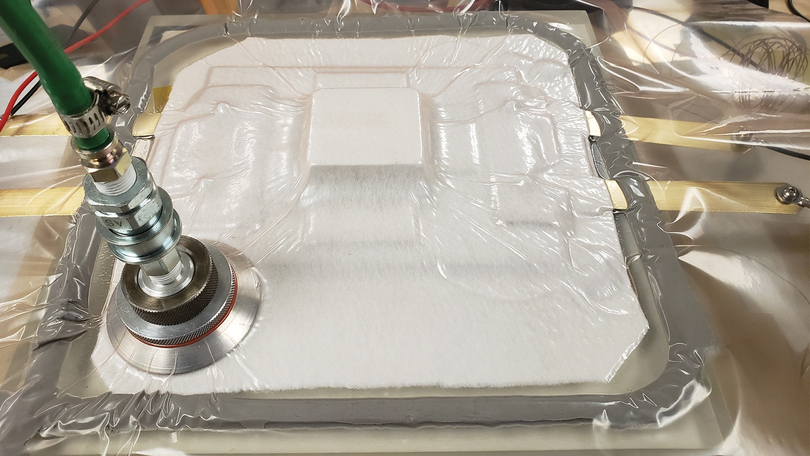 A manufacturing process image shows a vacuum seal system applied to a square component, with a green tube attached to the vacuum adapter. The component is encased in a clear plastic sheet.