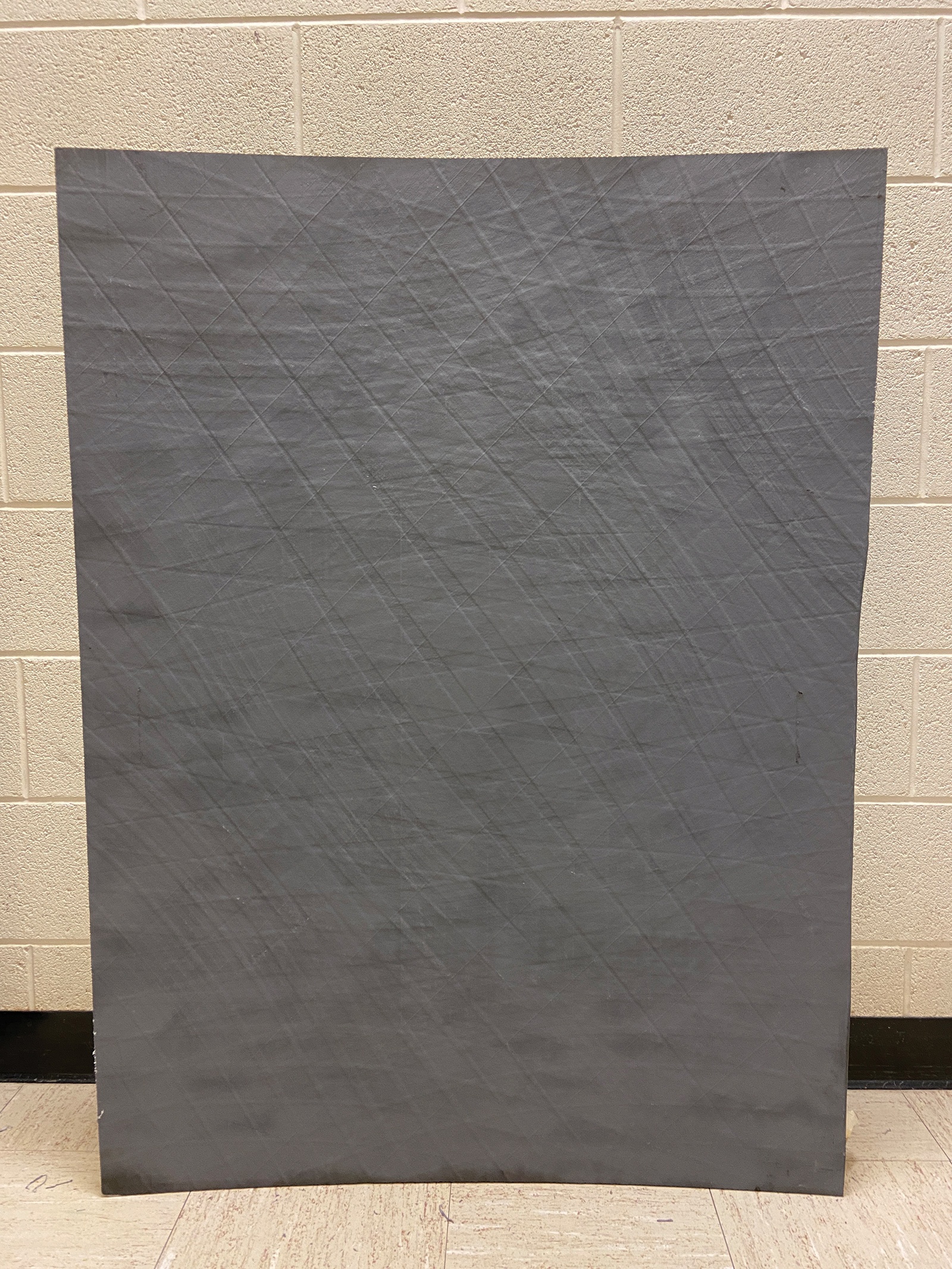 A large, rectangular piece of dark gray textured fabric is displayed against a beige brick wall and a light-colored tiled floor.