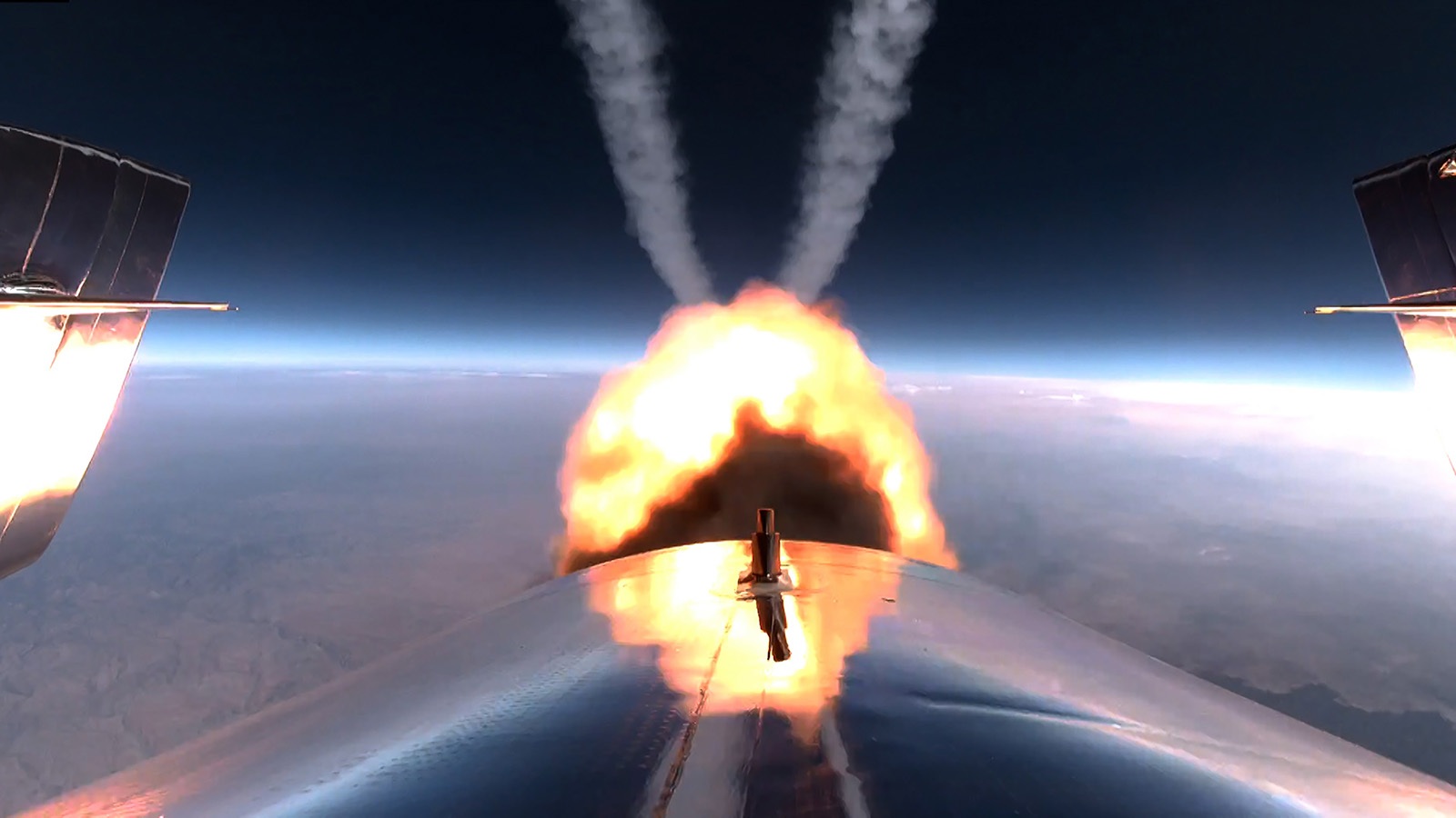 A rocket engine ignites in space with flames and smoke trailing behind, against the backdrop of Earth's curvature and the dark expanse of space.