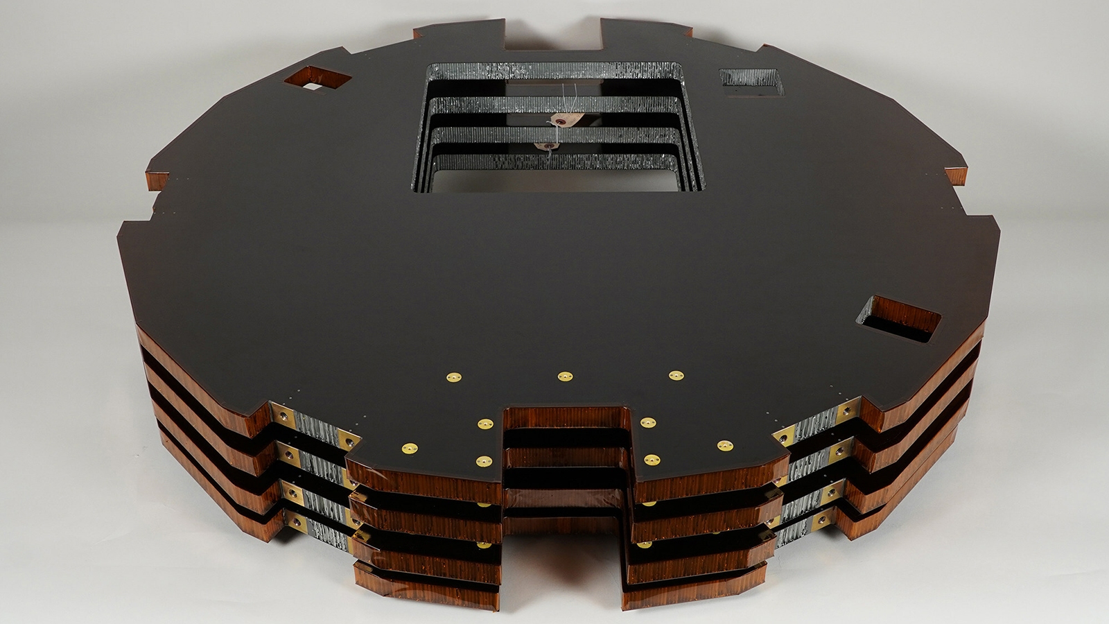 A stack of layered, dark-colored panels with cutouts, arranged in a stepped design, resting on a flat surface.