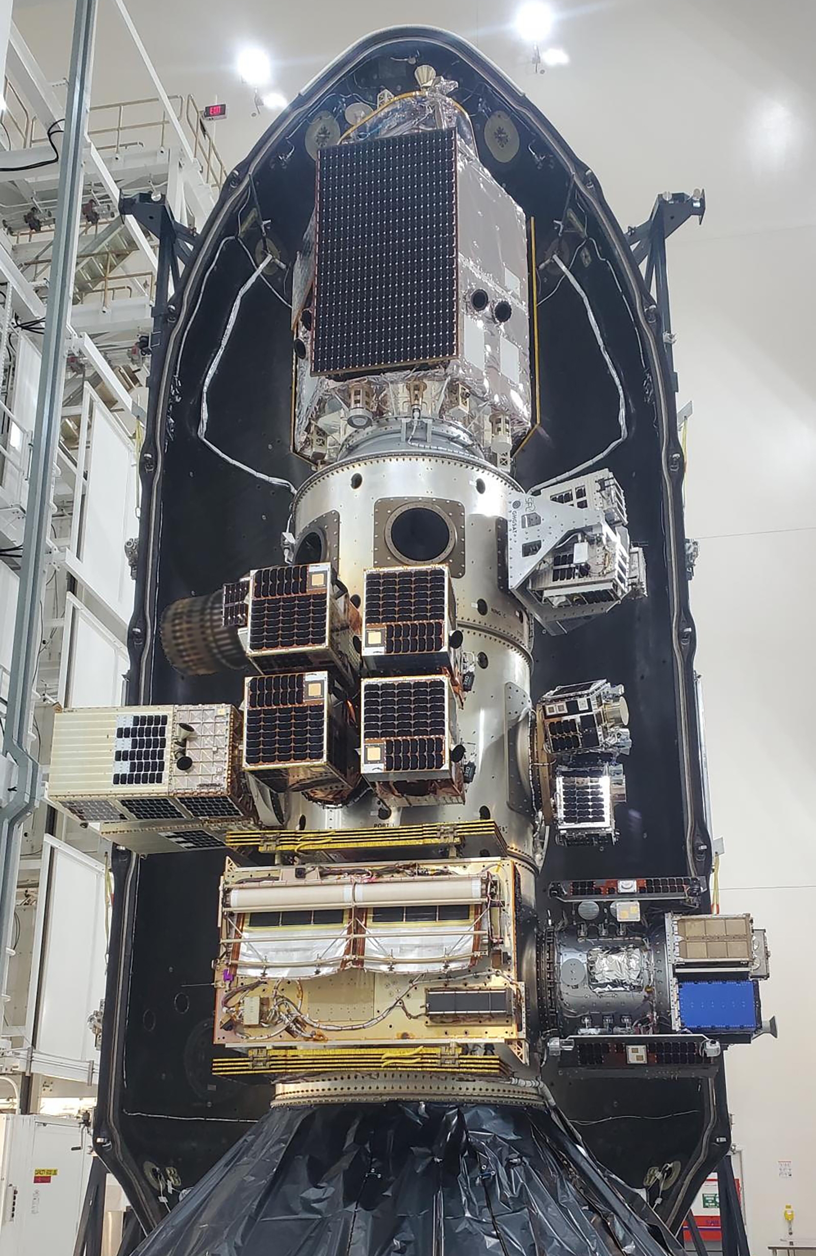 A close-up view of multiple small satellites securely mounted inside the payload fairing of a rocket, ready for launch. The setup is surrounded by a protective shell in an indoor facility.