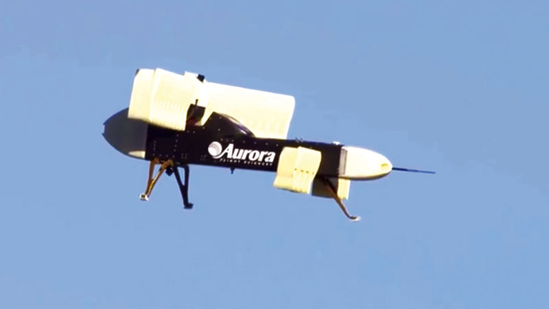A yellow and black unmanned aurora drone flying in a clear blue sky.
