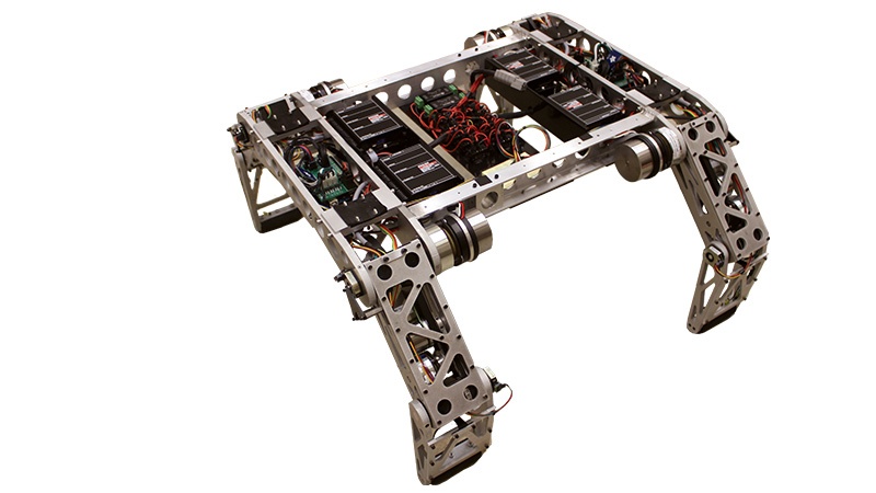 A four-legged robotic structure made of metal, featuring visible wiring and mechanical components, isolated on a white background.