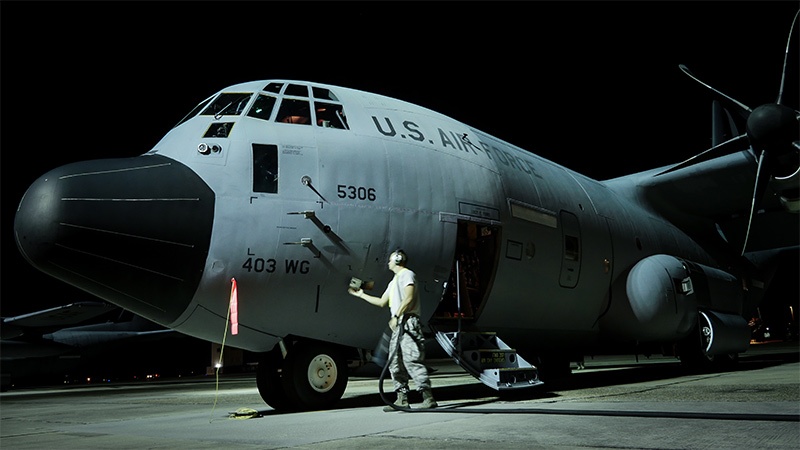 A u.s. air force serviceman stands by a large military cargo plane at night, holding a safety flag next to the open cargo door.