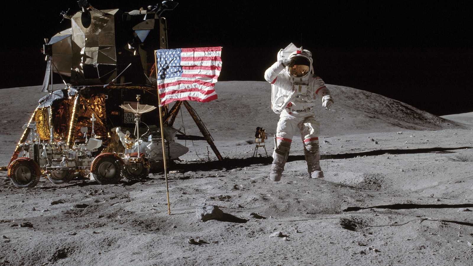 An astronaut in a spacesuit jumps on the Moon's surface near an American flag, a lunar rover, and a lunar module against a dark sky.