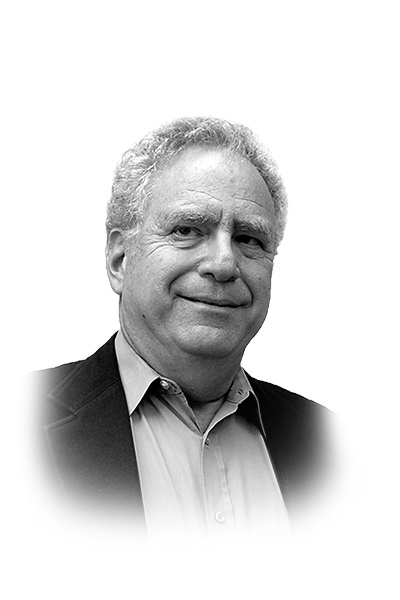 Black-and-white portrait of an older man with curly hair, wearing a button-up shirt and a blazer, looking slightly to the side with a neutral expression.