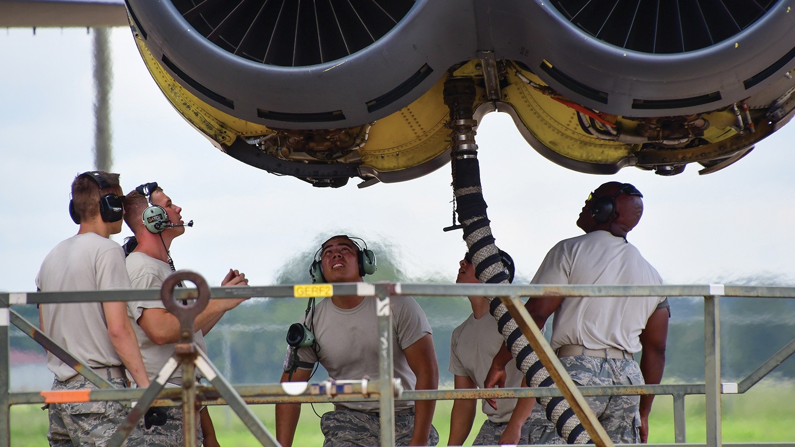 A group of people in military uniforms perform maintenance on the undercarriage of an aircraft.