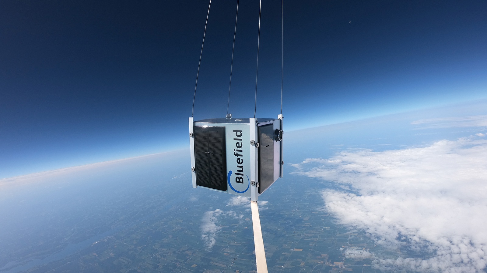 A Bluefield atmospheric data collection device is suspended mid-air above the clouds, with earth's horizon visible in the background.