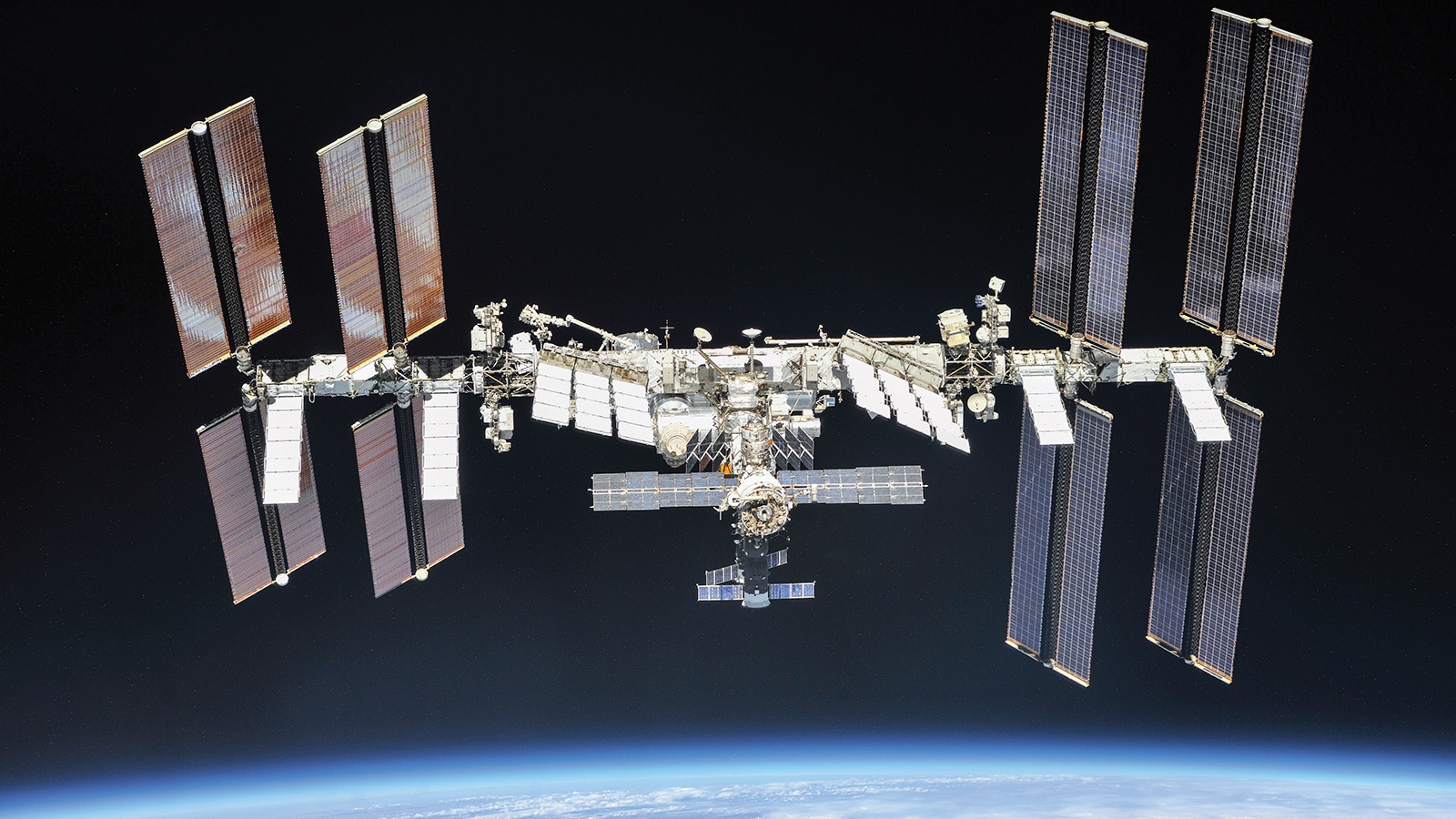 Image of the International Space Station floating above Earth with solar panels fully extended against the backdrop of space.