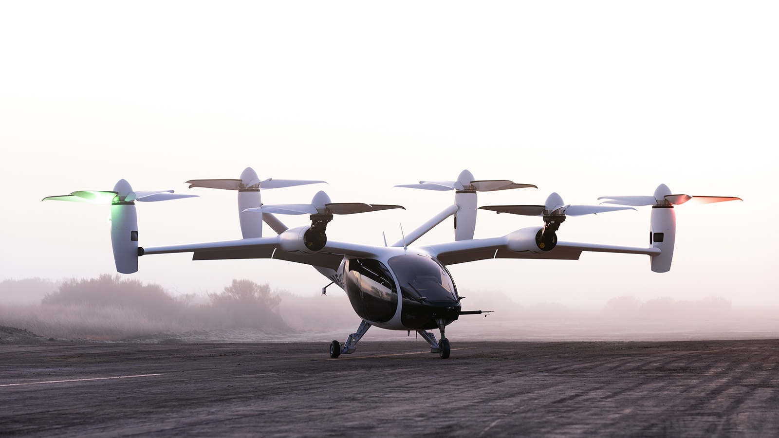 A six-rotor electric vertical takeoff and landing (eVTOL) aircraft is parked on a dirt surface with a misty, natural background. Two of the rotors are illuminated in green and red lights.
