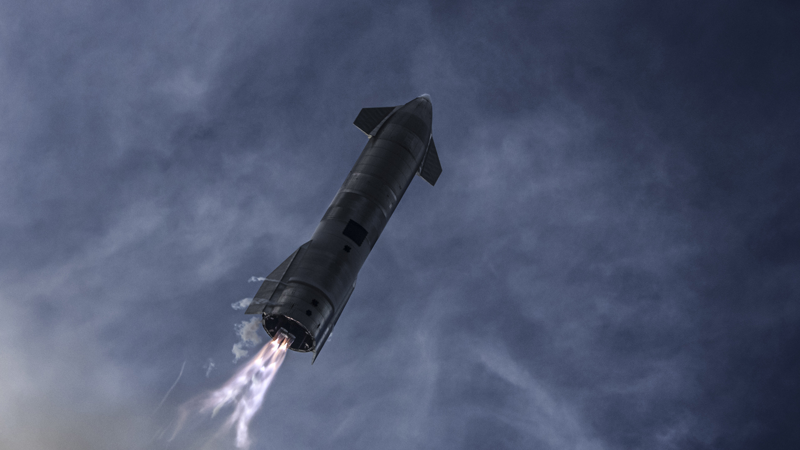 A rocket with fins is launched skyward, emitting flames and smoke from its engines against a dark, cloudy sky.
