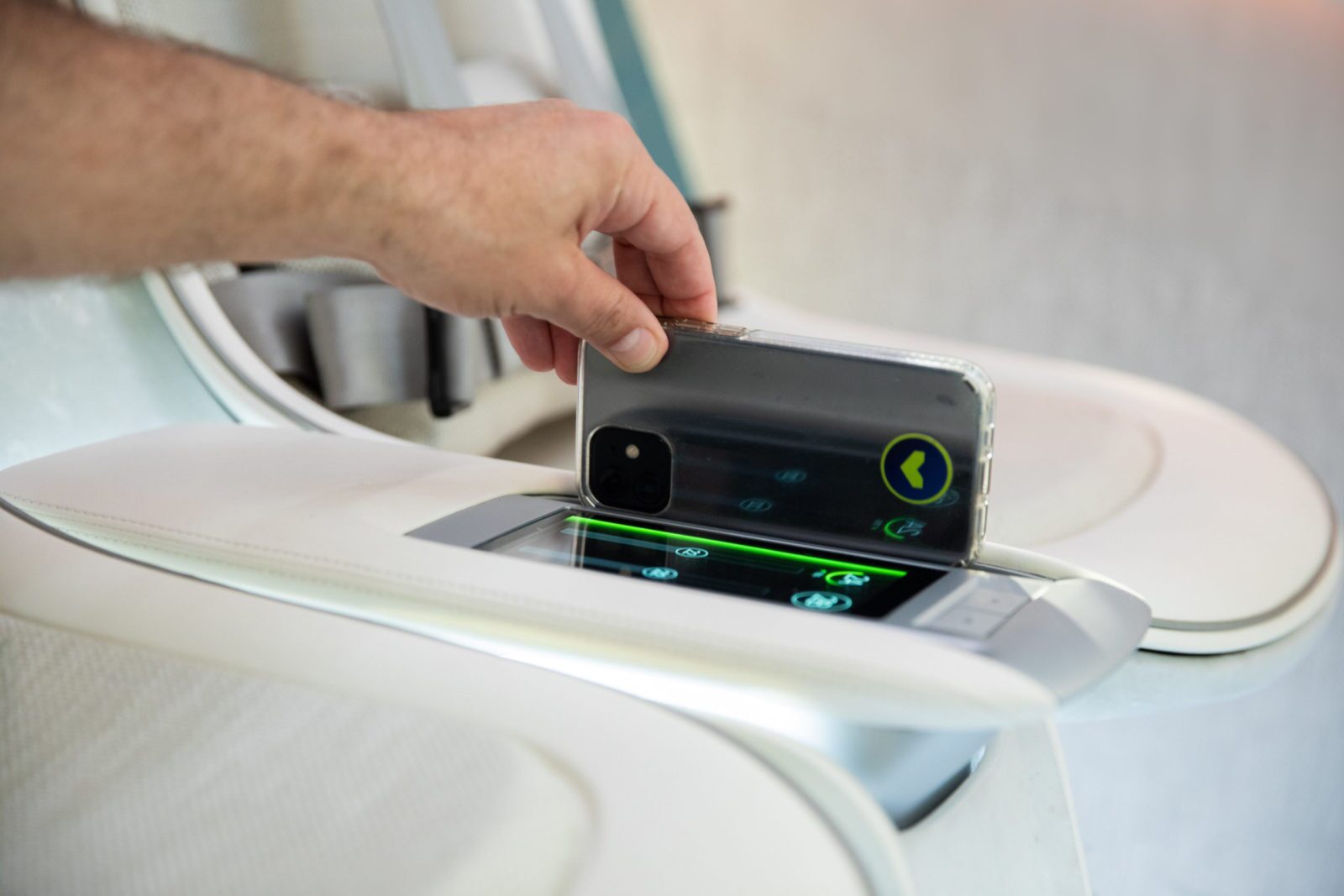 A person holds a smartphone over a wireless charging pad integrated into a white armrest.