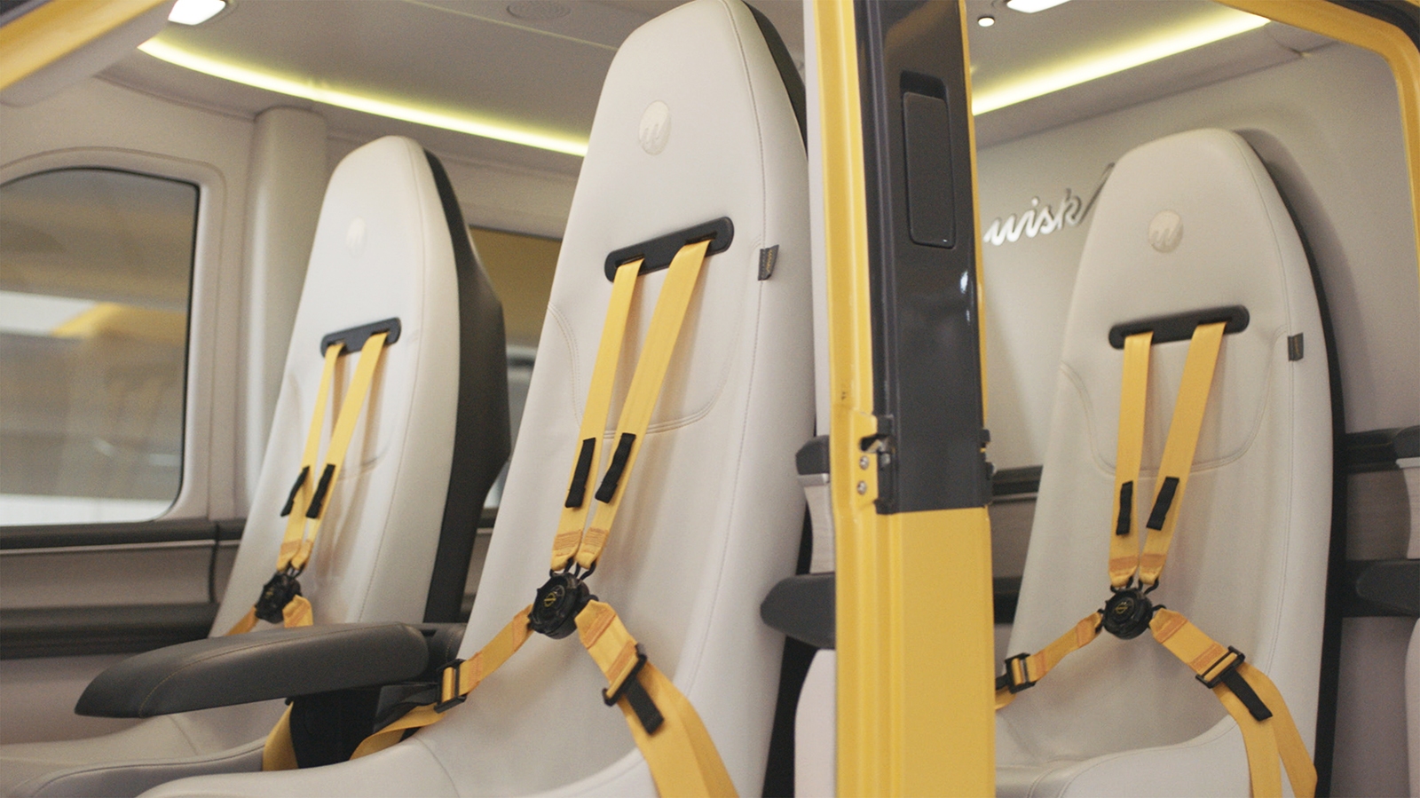 Interior view of a vehicle showing two white seats with yellow harnesses and black buckles inside an open door.