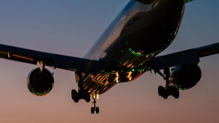 September 2024 AIAA Bulletin A commercial airplane approaches for landing at dusk with its landing gear extended and lights illuminated.