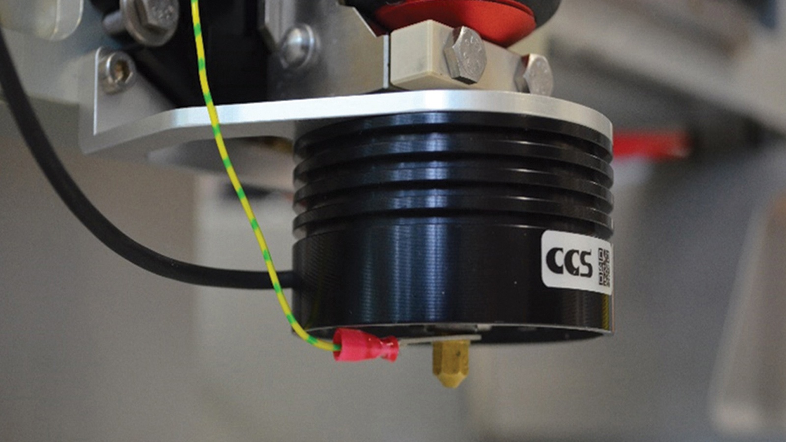 Close-up of a black and silver CCS sensor or component with connected wires, mounted on a piece of industrial machinery.