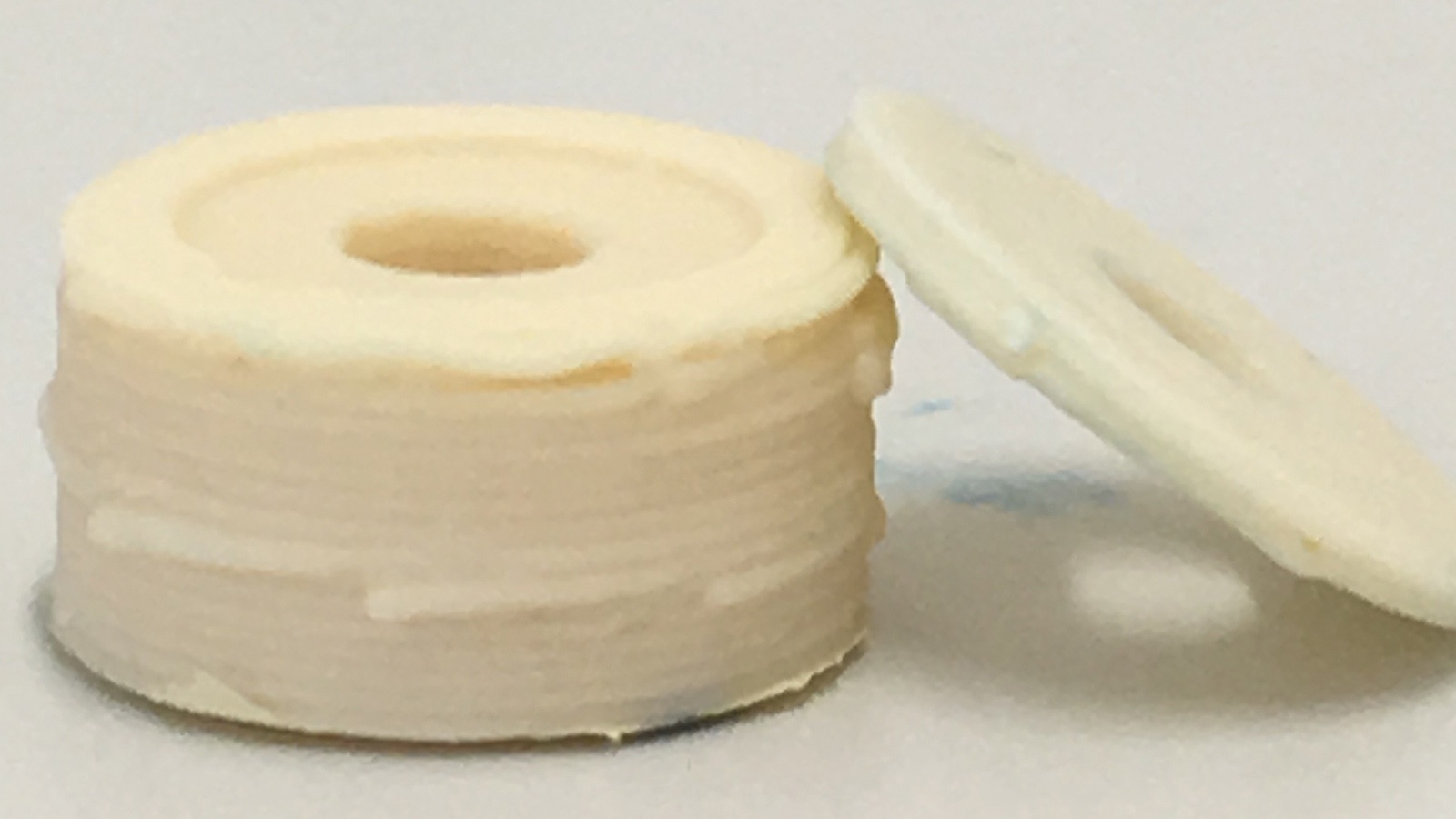 Two circular, cream-colored objects with central holes, one resting vertically and the other leaning against it, placed on a plain surface.