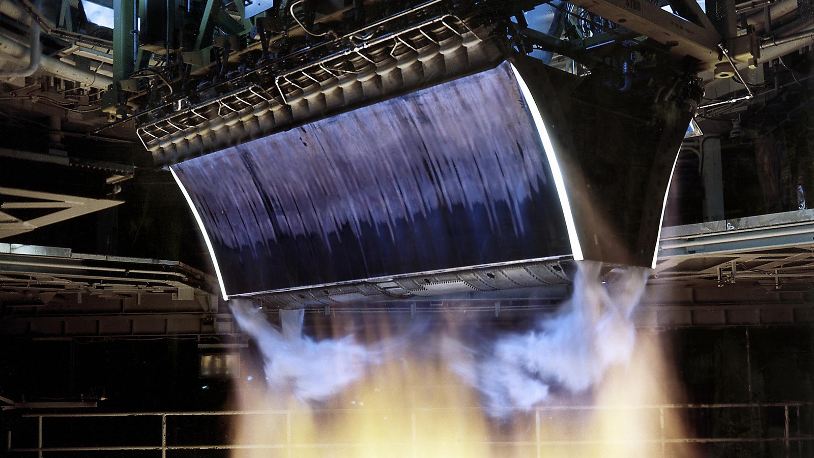 Close-up view of a rocket engine nozzle during a test firing, with flames and exhaust gases emanating from the engine.
