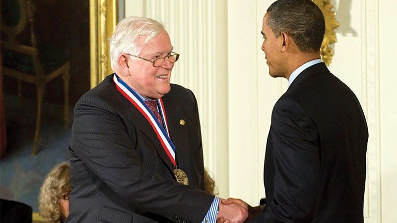 Former u.s. president barack obama shakes hands with an elderly man receiving a medal in a formal ceremony.