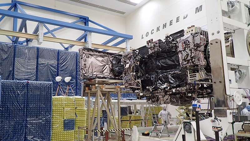 A satellite assembly at a lockheed martin facility with engineers working around it.