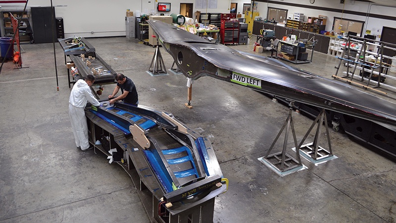 Two workers inspect aircraft parts in a spacious industrial workshop.