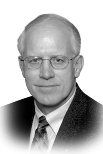 Black and white portrait of an older man with glasses, short light-colored hair, and a suit and tie. He is facing the camera with a neutral expression.