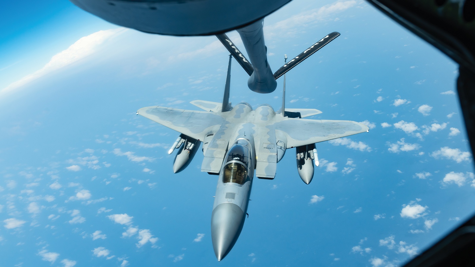 An F-15 fighter jet is being refueled mid-air by a tanker over the ocean on a clear day.