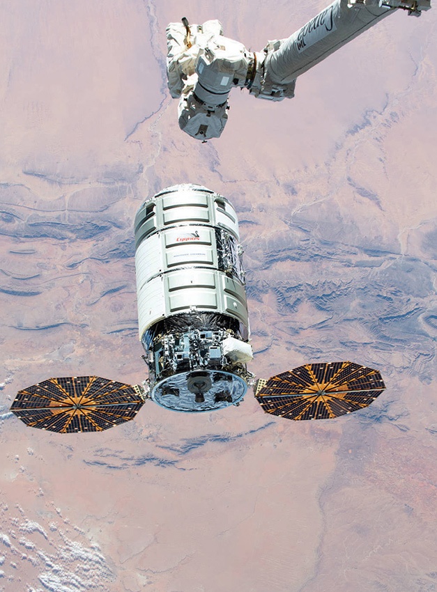 A spacecraft with two circular solar panels is being maneuvered by a robotic arm over a desert landscape.