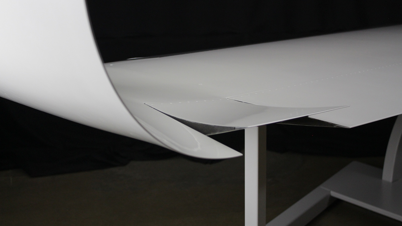 Close-up view of an aircraft wing's trailing edge with a sharp, streamlined design against a dark background.