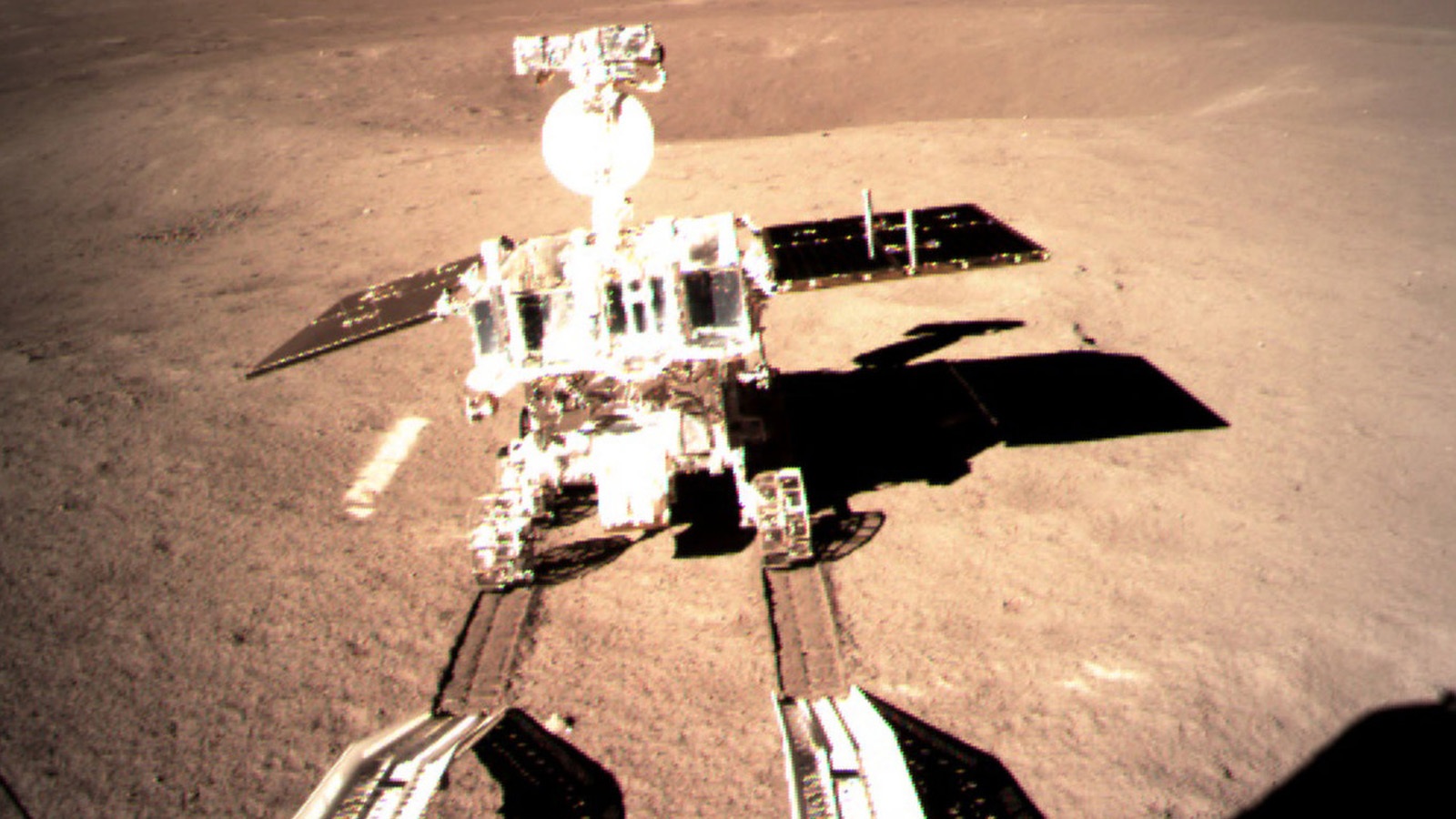 A rover with solar panels explores a barren, rocky surface under sunlight.