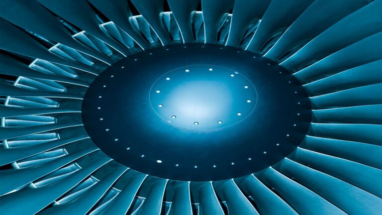 December 2023 AIAA Bulletin Close-up of an aircraft jet engine turbine, showing the circular fan blades and central hub, illuminated with a blue tint.