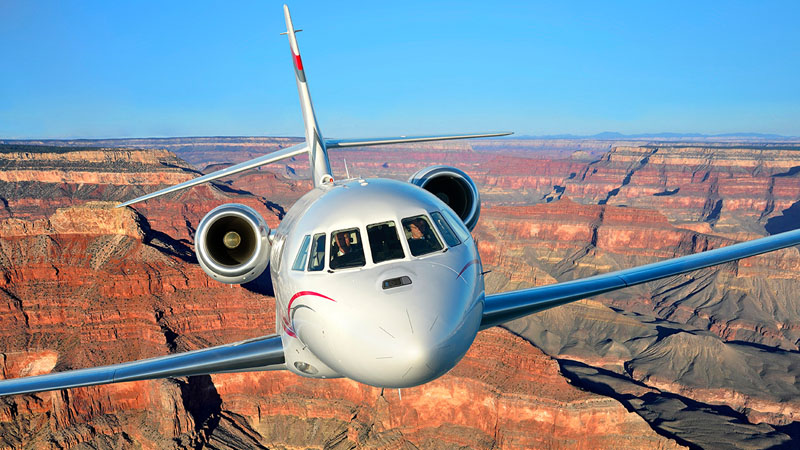 A private jet flying low over the grand canyon, showcasing a clear view of the red rocky landscape below.