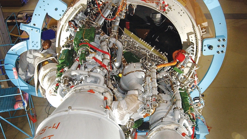 Engineers work on the intricate internal components of a spacecraft, surrounded by a large blue support structure.